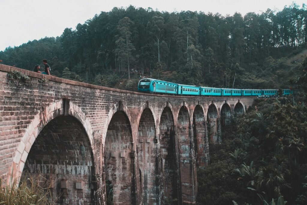 A blue train traverses the iconic Nine Arch Bridge in Ella, surrounded by lush Sri Lankan forests.